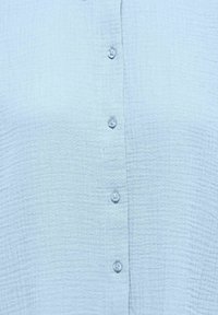 Lyseblåt tekstureret stof med en lodret række af seks matchende runde knapper centreret ned langs midten.