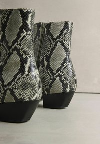 Ezüst és fekete kígyóbőr mintázatú bokacsizma, cipzárral és vastag sarokkal. Sima textúra, fényes felülettel.