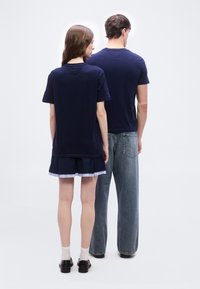 Δύο άτομα με την πλάτη στην κάμερα φορούν μπλε σκούρα πουκάμισα· το ένα φορά φούστα με μαύρα παπούτσια και κάλτσες, το άλλο άνετο τζιν και μαύρα παπούτσια.