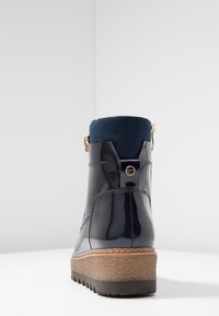 Stivaletto in pelle verniciata nera con tomaia in camoscio blu, caratterizzato da una zip decorativa dorata, suola testurizzata e un tacco a piattaforma robusto.