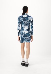 Φόρεμα με μακριά μανίκια σε σκούρο μπλε χρώμα με λευκά και ανοιχτό μπλε σχέδια. Στενή γραμμή με ψηλό λαιμό και λεπτομέρεια ραφής στην πλάτη.