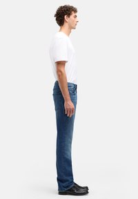 Niebieskie dżinsy denimowe o prostym kroju nogawki, z talią o średnim kroju, pięcioma kieszeniami i subtelnym spraniem. Połączone z gładkim białym t-shirtem i czarnymi butami.