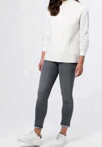 Witte geribbelde coltrui met lange mouwen, gedragen met slim-fit grijze jeans en witte sneakers met patroonaccenten op de hak.