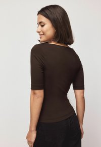 Brown, fitted top with short sleeves and a scoop neckline. Made of smooth fabric with a seamless design, paired with black high-waisted jeans.