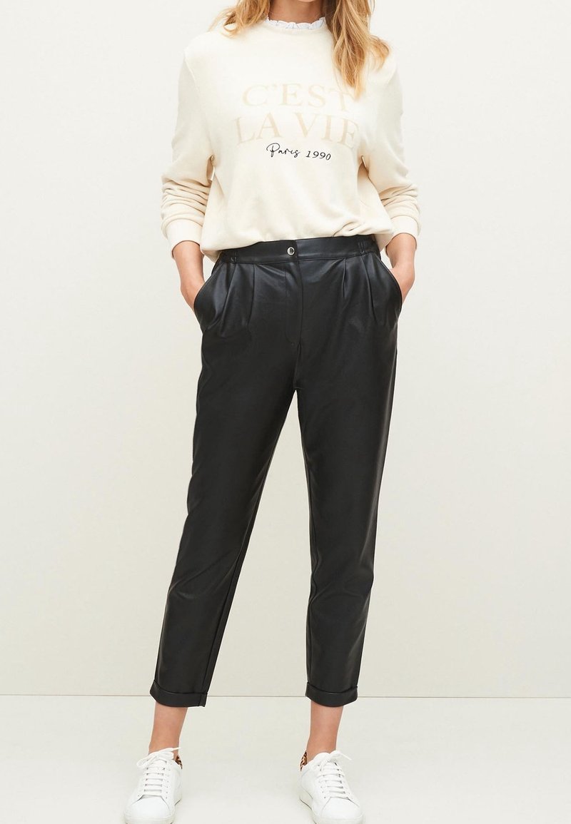 Czarne spodnie z ekoskóry z plisami, zwężanymi nogawkami i bocznymi kieszeniami, zestawione z kremową bluzą z nadrukowanym tekstem. Białe trampki.
