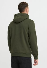 Haut en coton vert avec poche kangourou, poignets et ourlet côtelés. Dispose d'une capuche avec cordon de serrage et d'une finition unie et texturée.