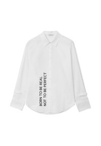 Chemise blanche à manches longues présentant un col classique, une fermeture à boutons et un design de texte sur le côté : "NÉ POUR ÊTRE RÉEL PAS POUR ÊTRE PARFAIT."