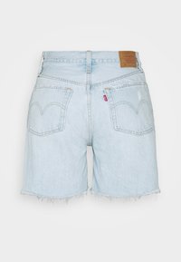 Short en denim bleu clair avec un ourlet effiloché, doté de deux poches arrière et d'une étiquette en cuir marron à la taille.