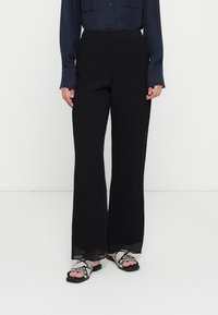 Zwarte, wijde broek gemaakt van textuurstof. Draag met zwart-wit slangenprint sandalen. Het shirt is marineblauw met knoopdetails.