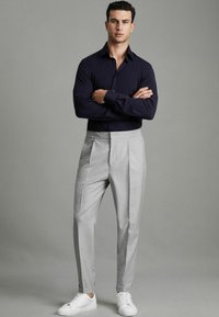 Cămașă albastru închis cu mânecă lungă, pantaloni gri deschis plisati, adidași albi. Cămașa are un guler clasic; pantalonii au o croială ajustată și tivuri răsucite.