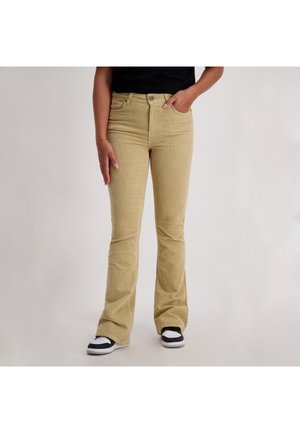 Beige corduroy flared jeans met voorzakken, een knoopsluiting en een gestructureerde afwerking, gecombineerd met zwart-witte sneakers.