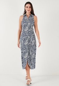 Navy blue, sleeveless midi dress with white leaf pattern, front buttons, and side slit, made from lightweight fabric. Worn with white shoes.