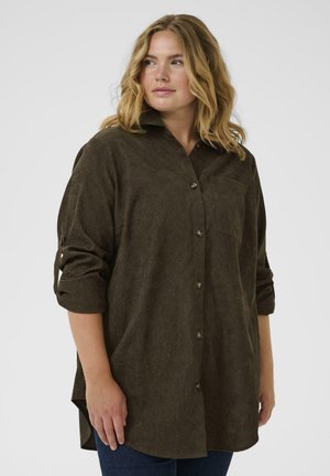 Chemise boutonnée marron foncé avec col, poche poitrine unique et manches retroussées. Texture douce et ourlet arrondi.