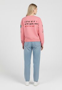 Felpa rosa con testo e grafiche sul retro. Abbinata a pantaloni azzurri testurizzati e sneaker bianche.