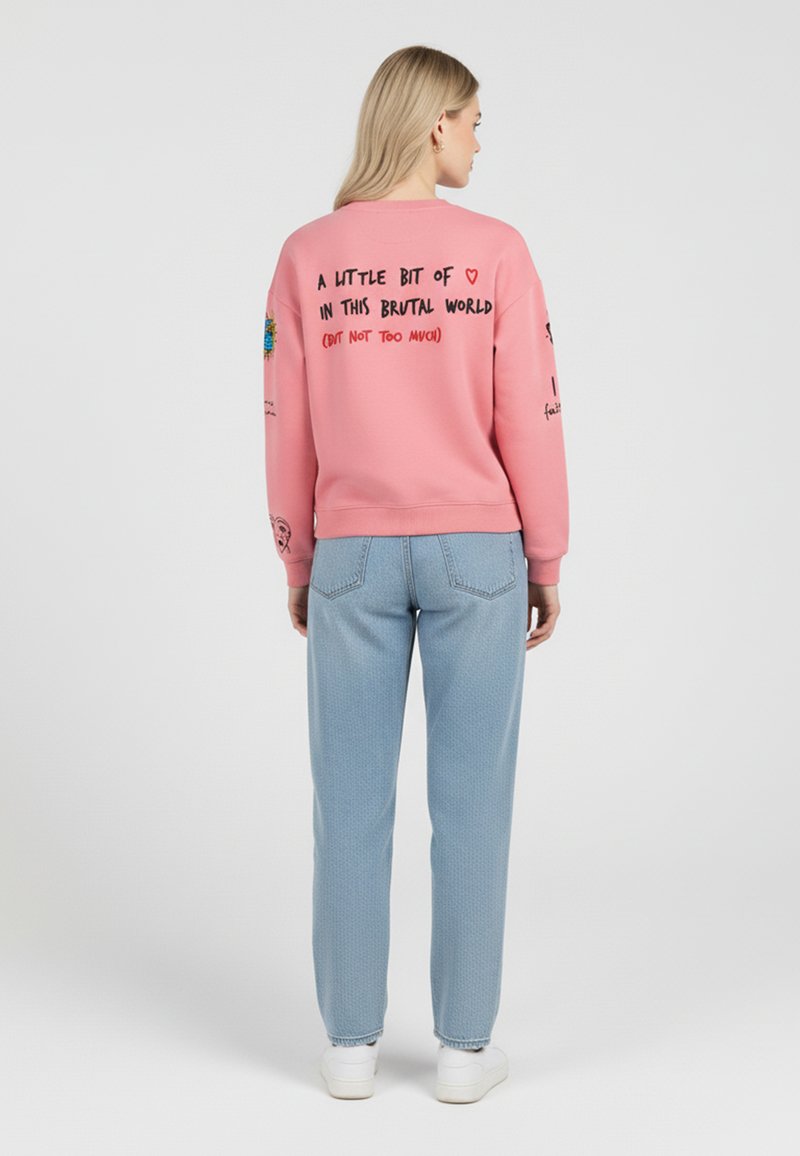 Felpa rosa con testo e grafiche sul retro. Abbinata a pantaloni azzurri testurizzati e sneaker bianche.
