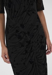 Čierne šaty s kvetinovým zamatovým vzorom, zrušeným dizajnom, pletenou tkaninou, krátkymi rukávmi a štruktúrovanými detailmi na bočnom šve.