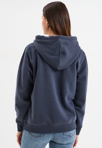 Hoodie bleu marine avec un cordon de serrage et une grande capuche, fabriqué en tissu doux. Présente des poignets et un ourlet côtelés, sans motifs ni logos visibles.