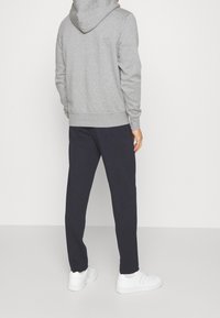 Felpa grigia con cappuccio e polsini a coste, abbinata a pantaloni scuri e sneaker bianche, che mostra un look casual e rilassato visto da dietro.