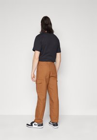 Bruna cargobyxor med sidofickor och rak benmodell, kombinerade med en svart t-shirt med kort ärm och svartvita sneakers.