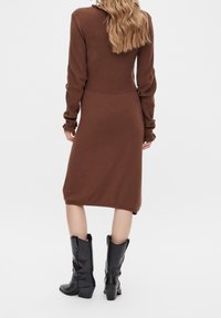 Brun stickad klänning med en figurnära överdel och något utsvängd fåll, med långa ärmar och textilstruktur. Matchad med svarta klackstövlar.