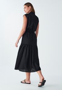 Czarna sukienka bez rękawów z kołnierzykowym dekoltem, z wcięciem w talii i warstwową spódnicą. Gładki materiał o zwiewnej sylwetce.