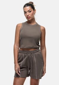 Top croppé marron avec des coutures claires, associé à un short assorti doté d'une taille élastique et de poches latérales. Texture lisse.