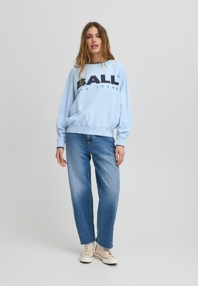 Lyseblå hettegenser med mørk trykk, avslappet passform, og ribbede cuff. Kombinert med lyseblå jeans og hvite sneakers med mønster.