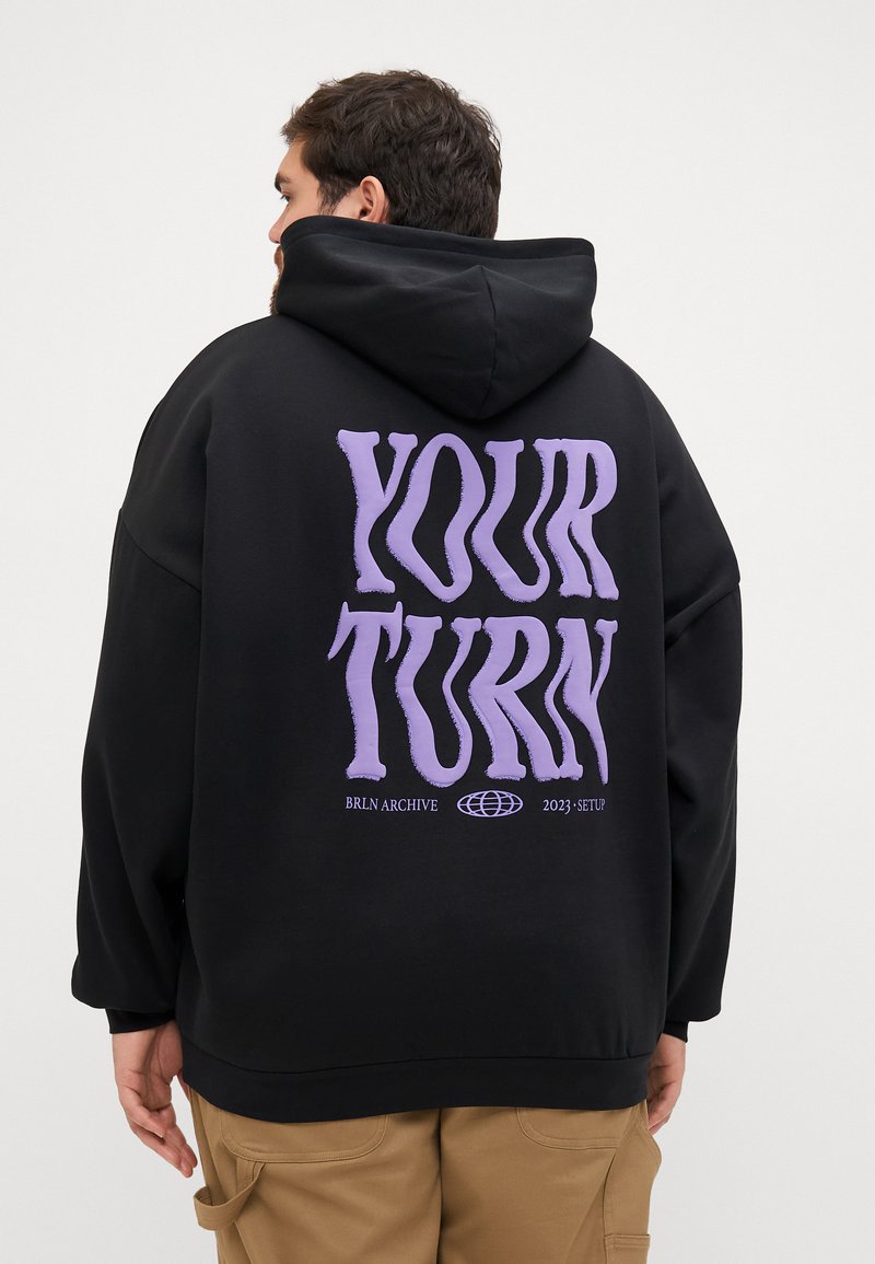 Felpa nera con cappuccio dal taglio oversize, grande scritta viola "YOUR TURN" sulla schiena e tasca a marsupio. Tessuto morbido in cotone misto.