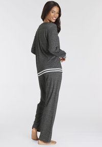 Graues Longsleeve-Oberteil und passende Hose mit weißen gestreiften Akzenten an den Bündchen und am Saum. Weicher Stoff, lockerer Schnitt und minimales Design.