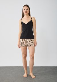Zwarte mouwloze top met een V-hals, gecombineerd met beige shorts met een zwart luipaardpatroon, een eenvoudige zoom en een relaxte pasvorm.