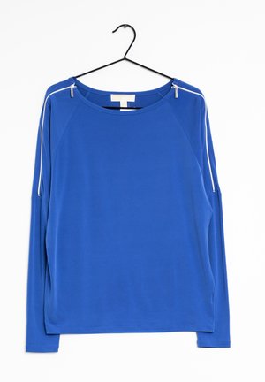 Haut bleu à manches longues avec des rayures blanches sur les épaules, un col rond et des détails zippés sur chaque épaule, accroché à un cintre noir.