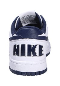 Sneaker Nike avec une base en cuir blanc, des accents bleu marine et un grand logo "NIKE" au talon. Langue texturée et semelle en caoutchouc robuste.