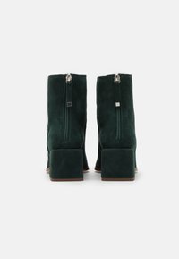 Botas de tobillo de ante verde con tacón cuadrado y cremalleras laterales. La textura suave y un diseño minimalista realzan el aspecto moderno.