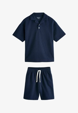 Tricou polo albastru închis cu mâneci scurte, doi nasturi și pantaloni scurți elastici asortați cu șnur alb în talie.