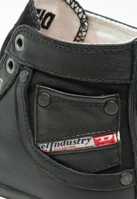 Czarne skórzane buty typu high-top z teksturowanym wykończeniem, z małą przednią kieszonką i widoczną metką marki wewnątrz. Metalowe oczka i detale szczytowe.