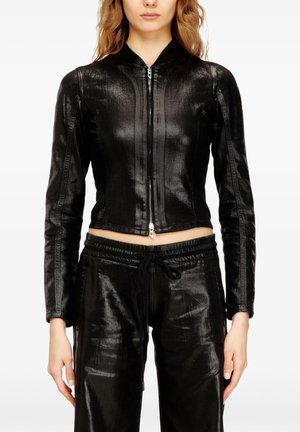 Donna che indossa una giacca nera lucida con cerniera e maniche lunghe e pantaloni neri con coulisse abbinati, mostrata dalle spalle ai fianchi.