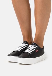 Mustad nahast spordijalatsid valgete paelte ja paksu valge tallaga. Küljel on punane Levi'si logo ning sujuv viimistlus.