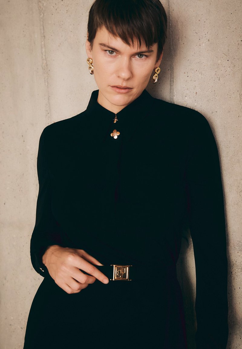 Black blouse with long sleeves, gold floral collar detailing, and a gold buckle belt featuring an embossed "F" logo. Smooth texture.