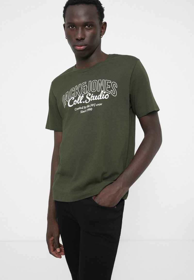 T-shirt en coton vert olive avec des manches courtes et un col ras du cou, présentant un texte graphique blanc en lettres grasses sur le devant.