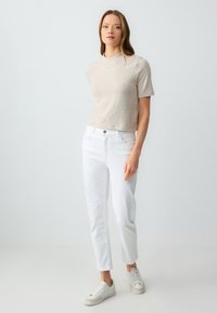 Maglietta corta beige chiaro con finitura texturizzata, abbinata a jeans bianchi aderenti e sneaker bianco sporco con dettagli beige.