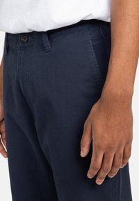 Navy blue cotton trousers with a straight cut, featuring a single button closure and side pockets, showcasing a smooth texture.