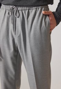 Graue Jogginghose mit weicher Textur, elastischem Bund, verstellbarem Kordelzug und Seitentaschen, die einen lockeren Schnitt und einen dezenten Glanz aufweist.