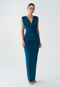 Sinakasharukas lõikega türkiissinine õhtukleit, külgmiste kortsude ja kõrge lõhikuga. Sile satiinriie, minimaalsete detailidega.