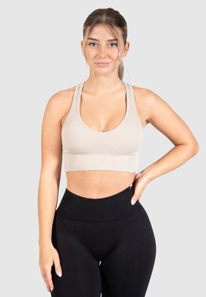 Beige ribbel sportbeha met brede bandjes, ronde halslijn en een aansluitend ontwerp. Gecombineerd met hoge zwarte leggings.