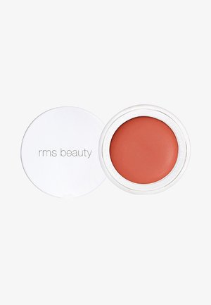 Crème blush in een ronde, witte compacte. De blush heeft een warme, gedempte oranje kleur met een gladde, matte textuur. Het deksel van de compacte heeft een logo.