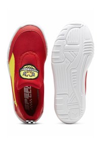 Punaiset kangaskengät keltaisilla yksityiskohdilla, pyöreä logo-patch ja valkoiset kumipohjat, joissa on teksturoitu uritus.