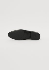 Talpa de pantof negru, cu o suprafață netedă și formă ascuțită. Prezintă o zonă texturată pentru aderență și un logo aproape de călcâi.
