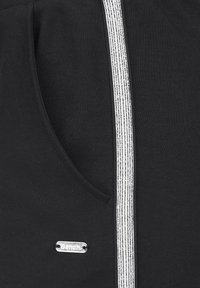 Black fabric with a vertical white double stitch line and a small silver "Bench" logo tag sewn near a pocket opening.
