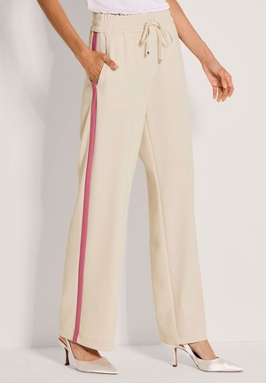 Beige Hosen mit weitem Bein, elastischem Bund, Kordelzug und pinken Seitenstreifen. Glatter Stoff mit Seitentaschen, kombiniert mit metallicfarbigen High Heels.