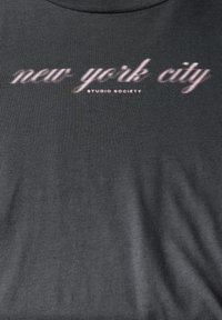 Tmavě šedá látka s růžovým kurzívním textem "new york city" a menším textem "STUDIO SOCIETY" pod ním.